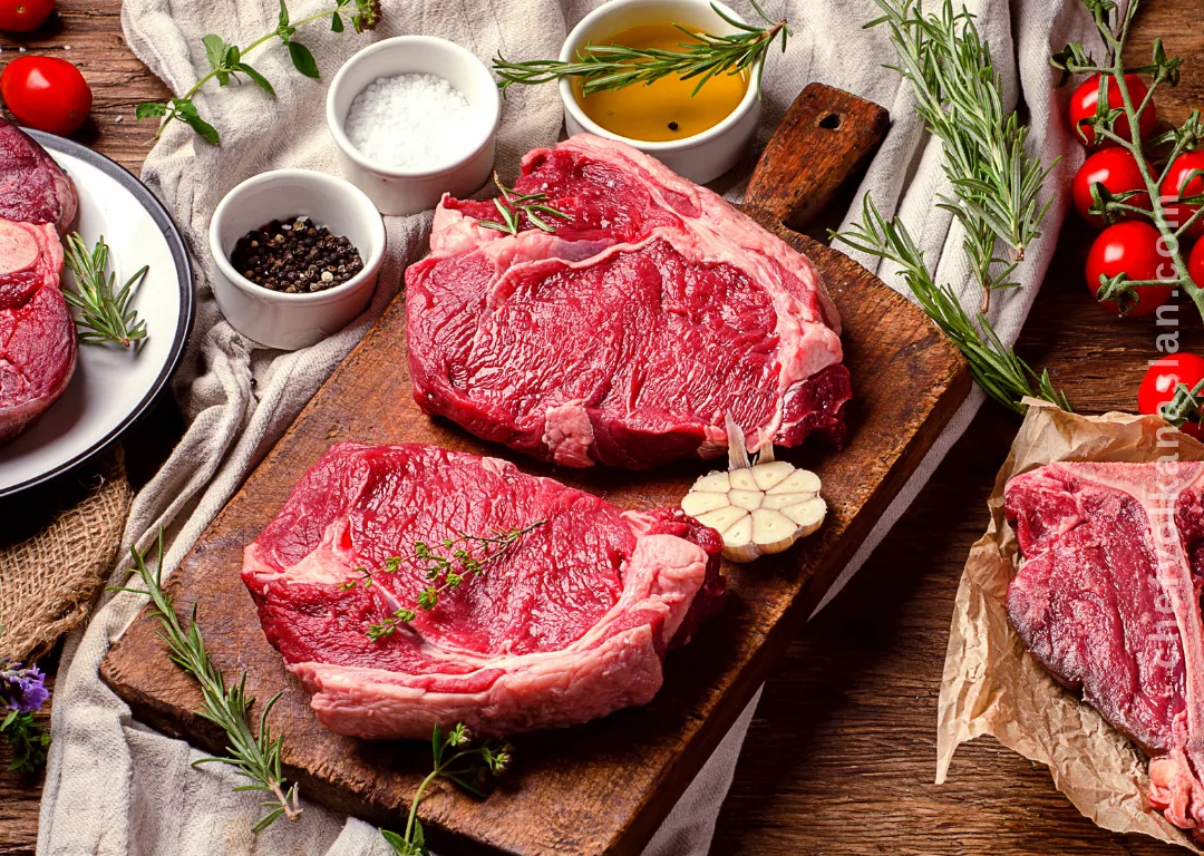 Raw red meat on a cutting board with herbs, spices and vegetables