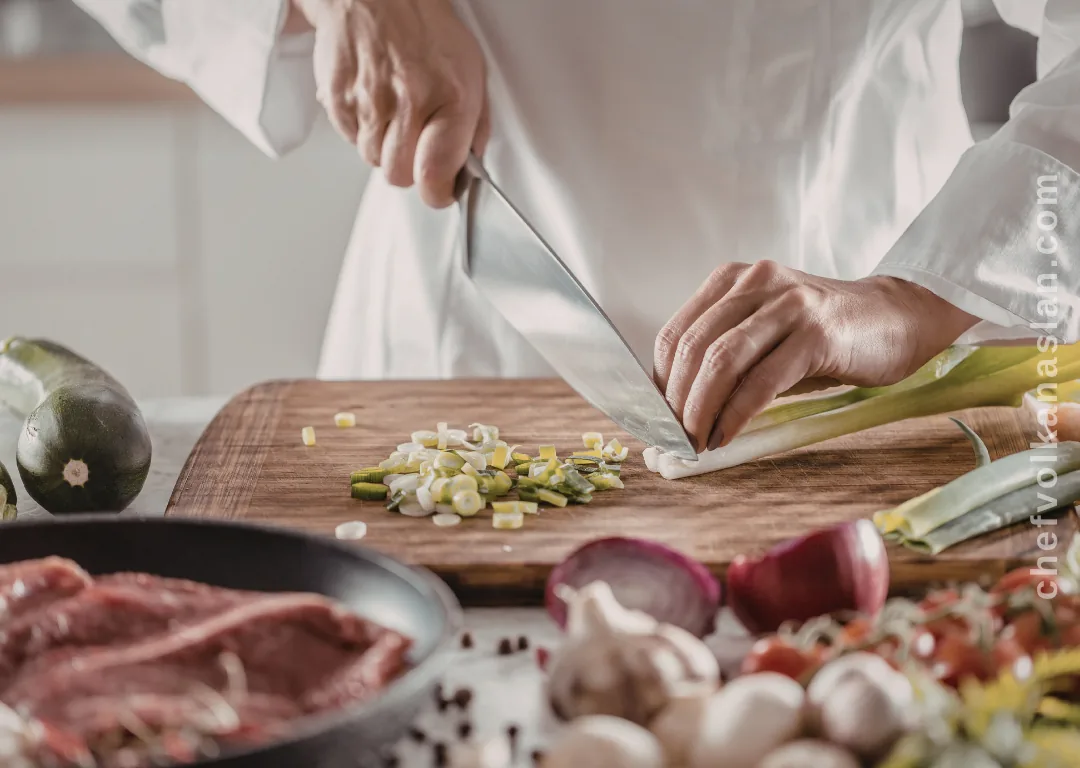 Hands chopping vegetables on a cutting board with a chef's knife